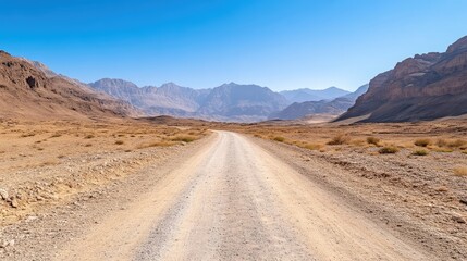 Naklejka premium Dusty road winding through a dry mountain valley under a clear sky