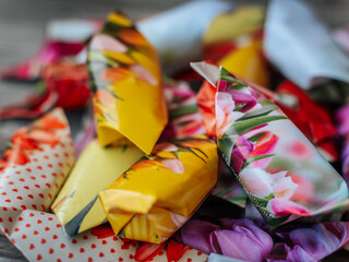 Bright close-up of assorted candies wrapped in floral themed paper in bright colors such as yellow, pink, red and purple. Arranged on a wooden surface. Skrīveri, Latvia - 07.04.2025
