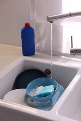 Dishes, blue sponge and foam under tap water in kitchen sink, closeup
