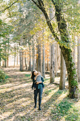 Obraz premium Smiling mother with a little girl in her arms walks through the forest