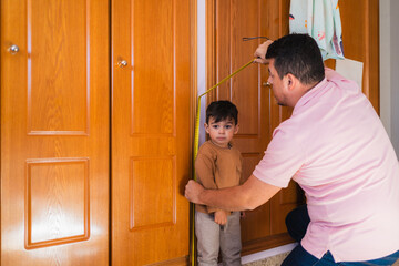 Father measuring his son's height with a tape measure on a wooden door frame, checking his growth progress