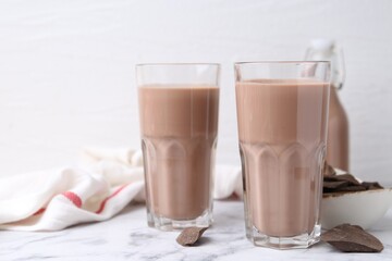 Tasty chocolate milk in glasses and pieces of chocolate on white marble table, closeup. Space for text