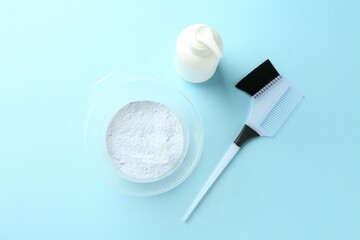 Bleaching powder and hairdresser's tools on light blue background, flat lay