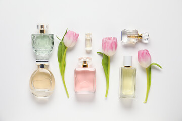 Bottles of aromatic perfume and beautiful tulips on white background, flat lay