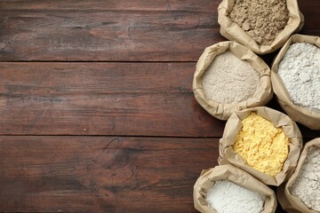 Different types of flour in paper bags on wooden table, flat lay. Space for text