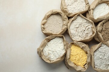 Different types of flour in paper bags on white table, flat lay. Space for text