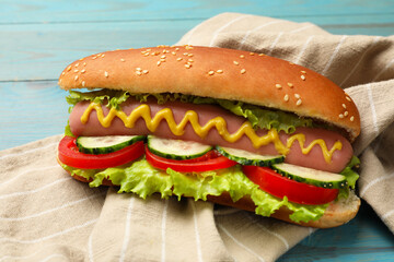 Tasty hot dog with vegetables on blue wooden table, closeup