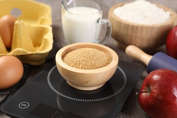 Digital kitchen scale with bowl of brown sugar and other products on grey table, closeup