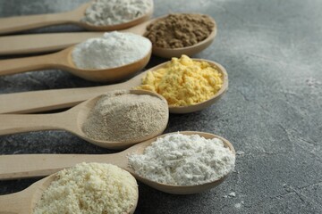 Different types of flour in spoons on grey table, closeup. Space for text