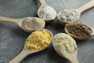 Different types of flour in spoons on grey table, closeup