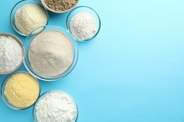 Different types of flour on light blue background, flat lay. Space for text