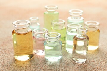 Perfume bottles with aromatic oils on beige textured background, closeup