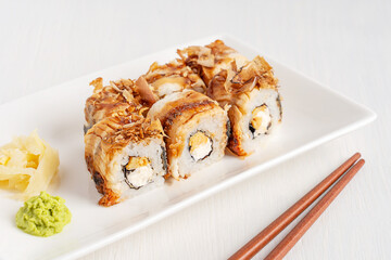 Homemade tasty juicy unagi sushi rolls topped with bonito flakes made from boiled rice, seaweed nori, fresh eel fish served with wasabi and ginger on plate on white wooden table with chopsticks