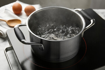Cooking pot with boiling water and stove on table against grey background, closeup
