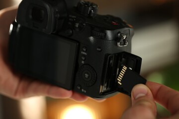 Man inserting SD memory card into photo camera indoors, closeup