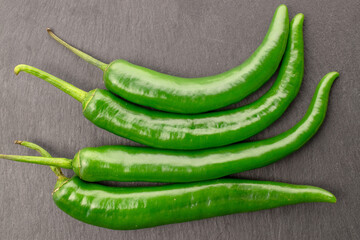 A few pods of ripe organic, spicy green hot pepper, close-up, on a serving plate of slate.