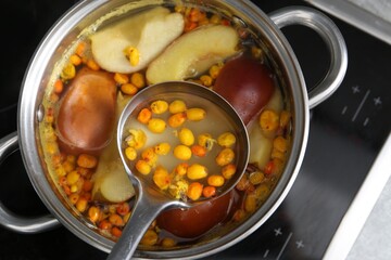 Taking tasty compot with ladle from pot on stove, top view