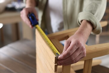 Man measuring wooden stool with tape indoors, closeup