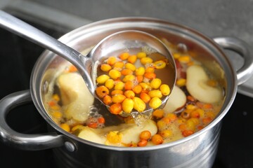 Taking tasty compot with ladle from pot on stove, closeup