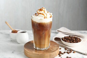 Tasty iced coffee with whipped cream, syrup and beans on white marble table