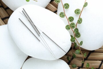 Acupuncture needles, spa stones and leaves on wicker mat, closeup