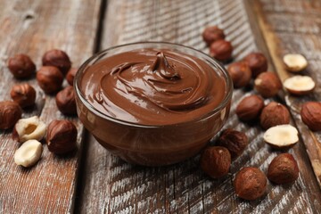 Chocolate hazelnut spread in bowl and nuts on wooden table, closeup