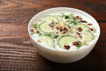 Tasty cucumber soup with dill and nuts in bowl on wooden table, closeup