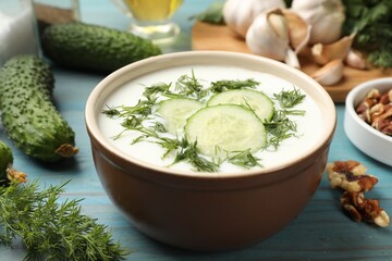 Tasty cucumber soup with dill among products on light blue wooden table, closeup