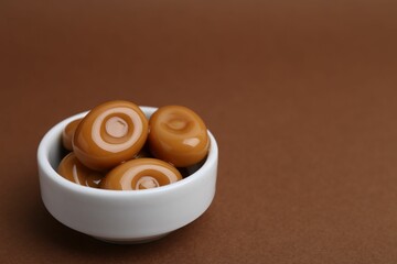 Tasty sweet caramel candies on brown background, closeup. Space for text