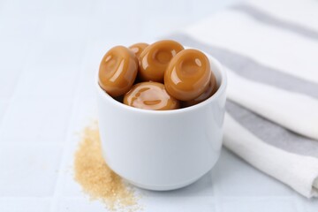 Tasty sweet caramel candies on white tiled table, closeup