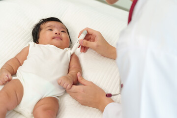 Asian pediatrician measuring underarm temperature of newborn baby boy using thermometer during checkup medical service concept child resting on white bedding pediatric care warmth health concern