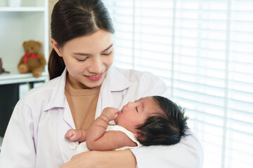 Fototapeta premium Female asian pediatrician holding newborn baby boy smiling gently making eye contact during hospital visit caring moment conveying warmth tenderness affection health support medical love concept