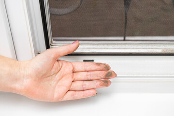 woman shows dirt accumulated on window, close-up. dirty plastic window. dust on the window. dirty mosquito net on the window