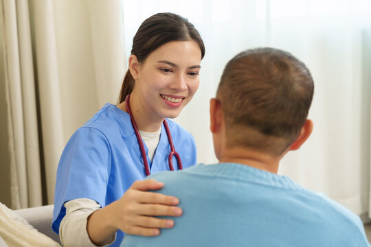 Young asian female physical therapist smiling kindly touching shoulder of elderly female patient during recovery session on sofa creating connection therapeutic relationship trust and encouragement