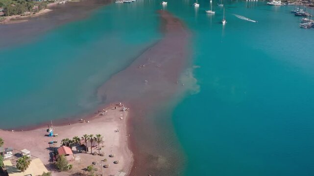Drone descending towards people walking in the shallow waters at the unique Kızkumu Beach. The walking path formed by the red sands and turquoise waters, an extraordinary beach.