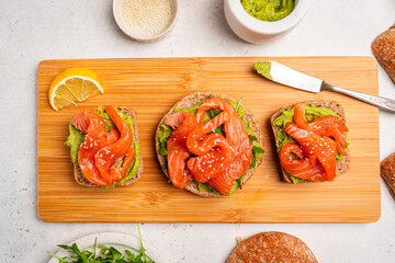 Avocado salmon sandwich or toast on rye bread with guacamole sauce, arugula and sesame seeds, white background, top view. Healthy food concept.