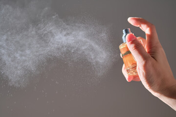 The hand sprays perfume from a transparent rounded bottle.