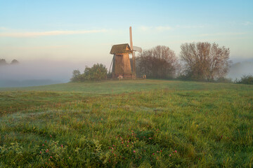 View of an ancient wooden windmill on the banks of the Sorot River on a foggy summer morning,...