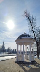Rotunda on left bank of Orlik River with beautiful view of Cathedral of Archangel Michael in Orel city. Old white gazebo on background of river and Orthodox church on sunny winter day