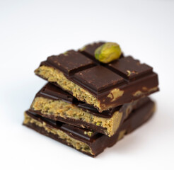 Stacked layers of kadaif embrace a generous coating of rich chocolate and are topped with a pistachio, showcasing the delightful texture and flavors in a culinary presentation.