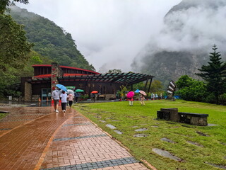 Visitors with umbrellas navigate the wet paths towards a visitor center in misty Taroko National Park Taiwan