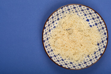 A patterned bowl contains a pile of freshly grated horseradish on a solid blue surface