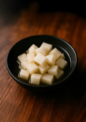 "Chicken mu", korean pickled white radish cubes in ceramic bowl on wooden table 