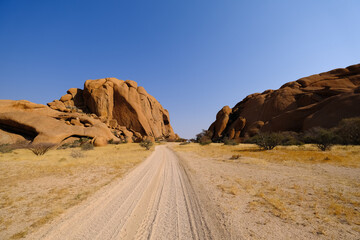 Sandy track winding between massive granite outcrops in Damaraland, under a clear blue Namibian sky.