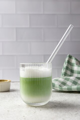Glass of iced matcha latte with reusable glass straw on kitchen counter