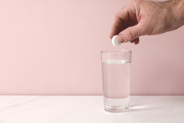Man dropping effervescent tablet into glass of water on pink background