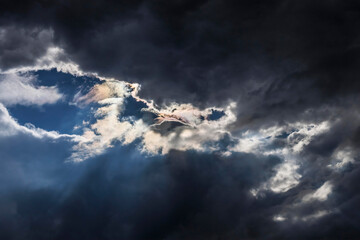 Dramatic sky with dark clouds and a glimpse of sunlight breaking through at dusk in a serene...