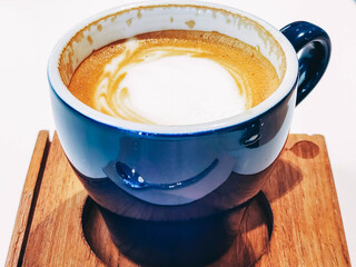 Cup of hot coffee with milk for breakfast indoor close-up. Creamy beverage in cafe. Coffeeshop. Latte coffee in a blue mug.  