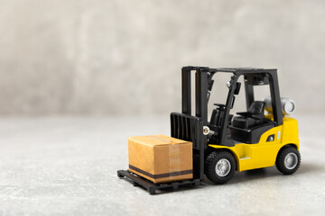 Yellow forklift on bright textured background. Logistics concept. Logistics and supply chain management for online shopping concept. Delivery of goods or products to the store worldwide. Cardboard box