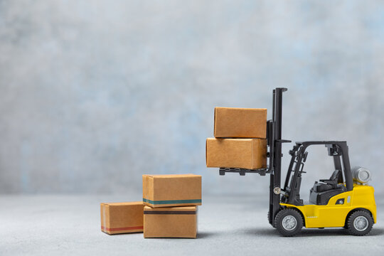 Yellow forklift on bright textured background. Logistics concept. Logistics and supply chain management for online shopping concept. Delivery of goods or products to the store worldwide. Cardboard box